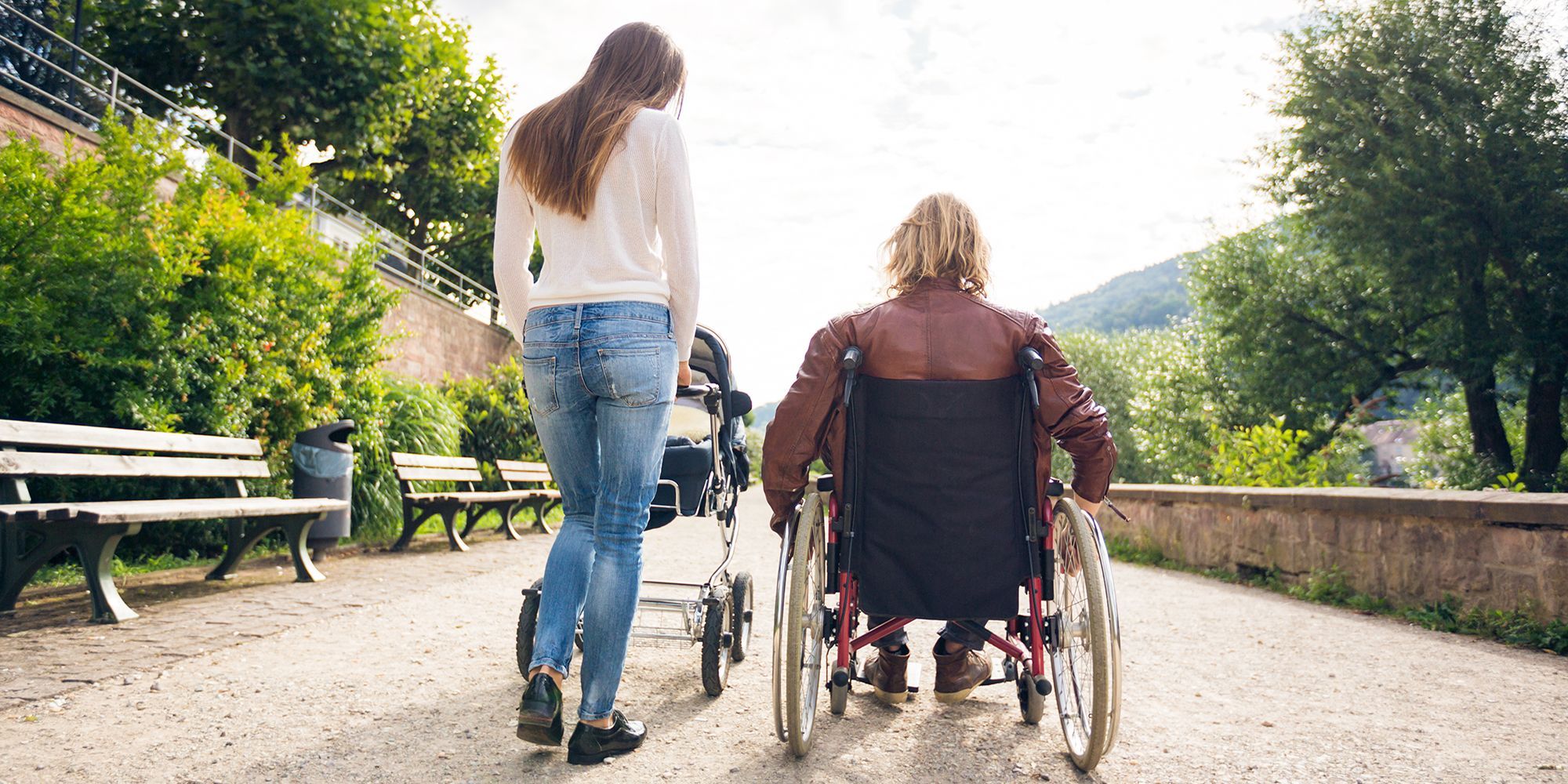 Mutter mit Kinderwagen geht spazieren mit Frau im Rollstuhl