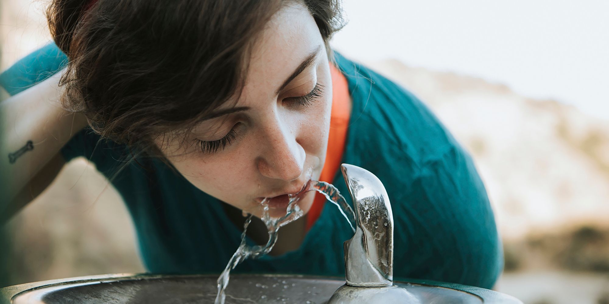 Junge Frau trinkt aus Wasserspender